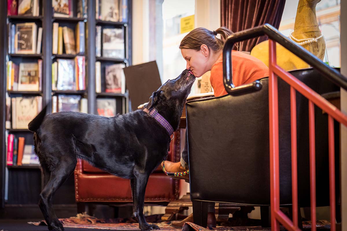 woman in a coffee shop with her dog who's giving her kisses