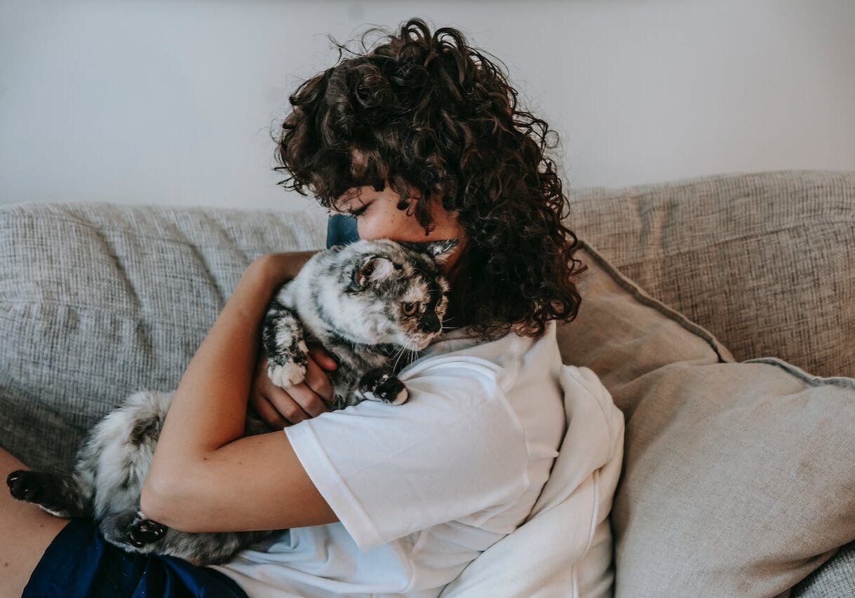woman laying on the couch while hugging her cat